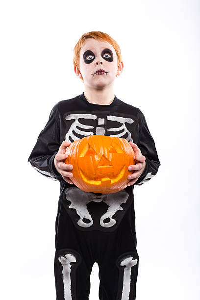 istock Red haired boy in skeleton costume holding a pumpkin. Halloween 519556127