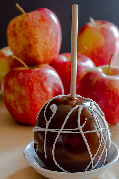 Homemade caramel apples with white chocolate drizzle sitting on small white plate with red apples