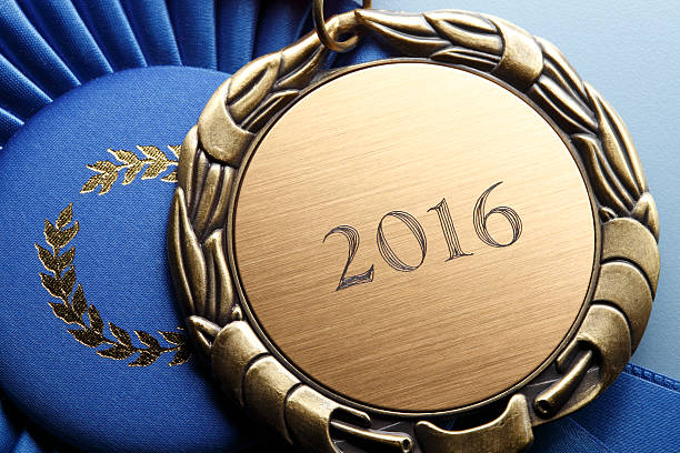 Gold Medal Engraved With 2016 Resting On Blue Ribbon A close up of a medal that is engraved with the year "2016" rests on top of a blue ribbon. 2016 stock pictures, royalty-free photos & images