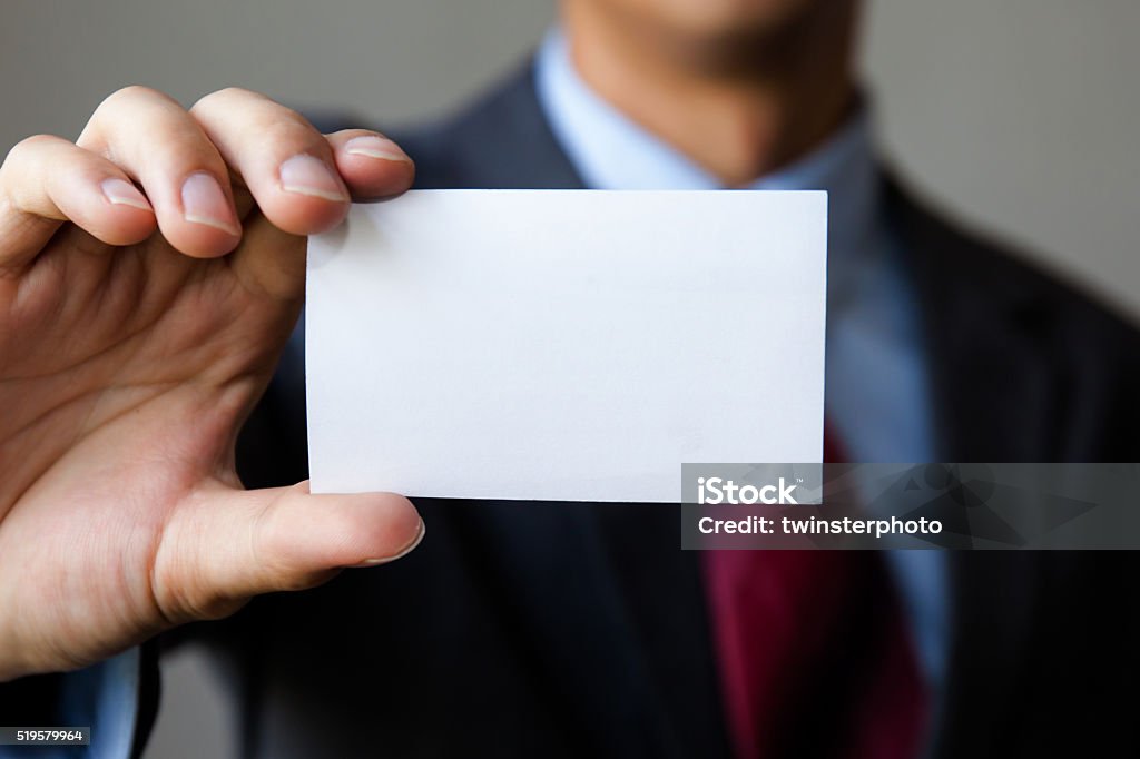Young man in business suit holding white blank business card Young man in business suit holding white blank business card. Business name card presenting (mock up white card) Adult Stock Photo