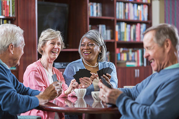 Multiracial group of seniors talking, playing card game A happy multi-ethnic group of seniors talking and playing a card game. An African American woman and her Caucasian friend are facing two senior man, laughing. friends playing cards stock pictures, royalty-free photos & images