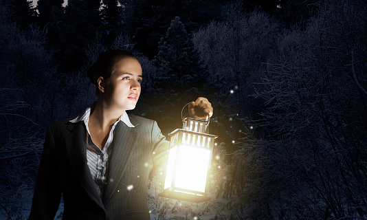 Young pretty businesswoman with lantern in darkness