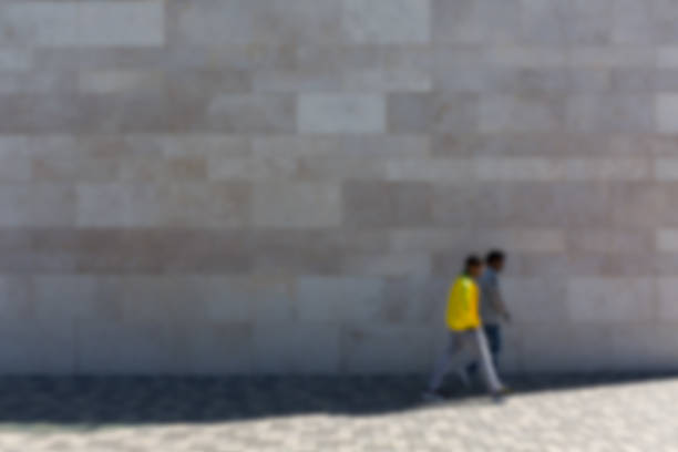 People in front of stone wall on pedestrian path, blurred, picture background