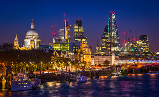 The historic dome of St. Paul's Cathedral and the futuristic skyscrapers of the City illuminated at dusk above the tranquil waters of the River Thames in the heart of London, the UK's vibrant capital city. ProPhoto RGB profile for maximum color fidelity and gamut.