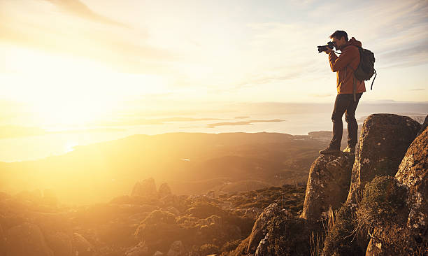 Capturing a beautiful view Shot of a young man taking pictures from the top of a mountain photographer stock pictures, royalty-free photos & images