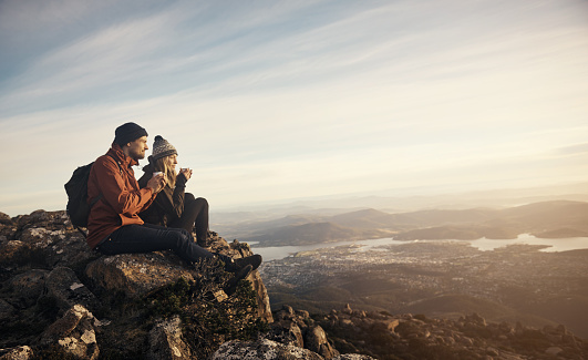 Shot of a young couple having coffee while looking down at the view from a mountain top