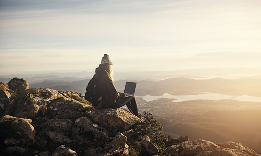 Shot of a young hiker using her laptop while sitting on top of a mountain