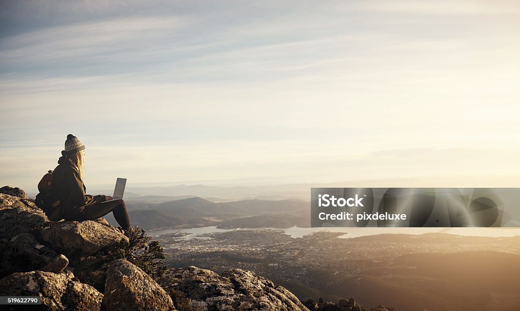 Time to check in... Shot of a young hiker using her laptop while sitting on top of a mountain Laptop Stock Photo