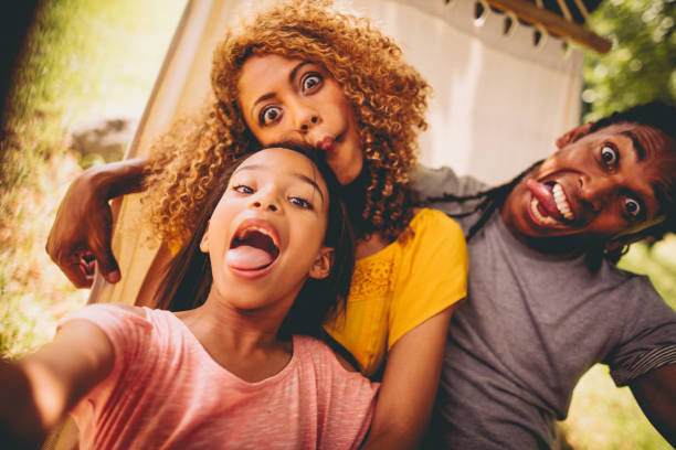 Lovely African-American family making silly faces and posing Attractive Multi-ethnic mother and father spends quility time with their adorable daughter, taking wacky selfies and swinging around on a hammock outdoors in nature. making a face stock pictures, royalty-free photos & images