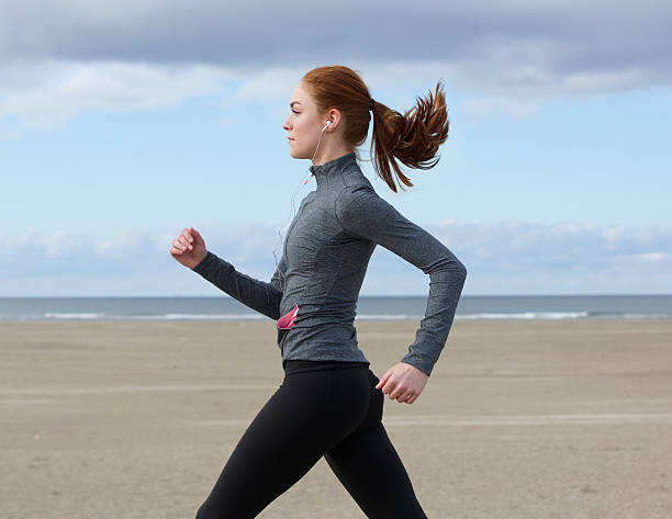 Young woman running by the beach Side view portrait of a young woman running by the beach power walking photos stock pictures, royalty-free photos & images