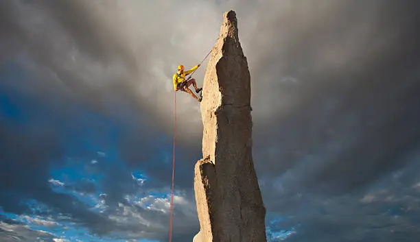 Climber struggles for his next grip on the edge of a challenging cliff.