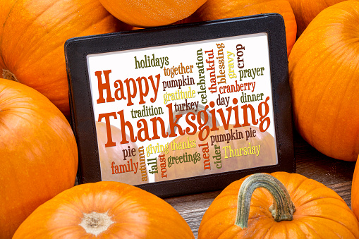 Happy Thanksgiving word cloud on a digital tablet surrounded by pumpkins