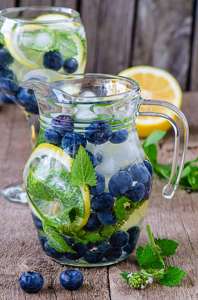 Refreshing drink with blueberry, mint and lemon, Refreshing drink in a glass jug with blueberry, mint and lemon, with ice on the wooden table blue jug stock pictures, royalty-free photos & images