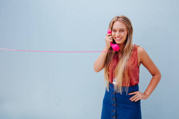 Young blonde girl talking on retro telephone Young girl with long blond hair talking on the pink phone, isolated on blue wall background girl flex stock pictures, royalty-free photos & images