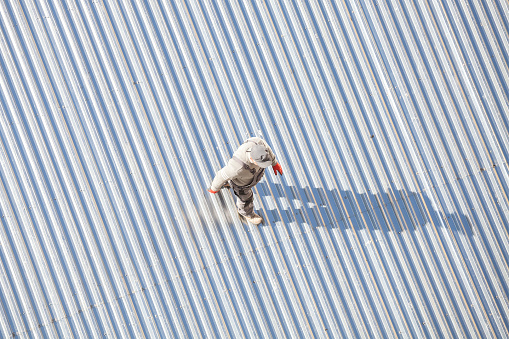 Szczecin, Poland - April 07, 2016: Man inspecting a roof made of corrugated metal sheets after repair, picture taken from above.