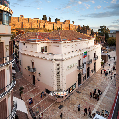 Malaga, Spain - March 20, 2016: view from a roof on the pedestrian zone of Alcazabilla, the cinema and further up the Alcazaba in the orange light of the setting sun; it is a chilly evening in spring so all pedestrians wear warm clothing. 