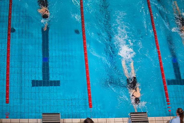 Swimmers butterfly swimming technique racing in a competitive swimming pool, creating splashes as they move powerfully through separate blue lanes