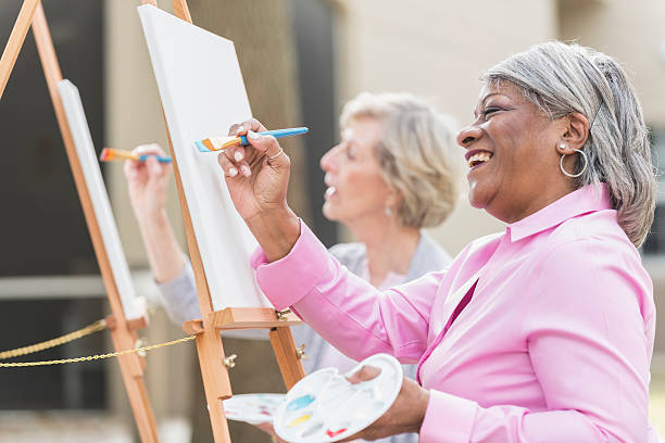Two senior women having fun painting in art class