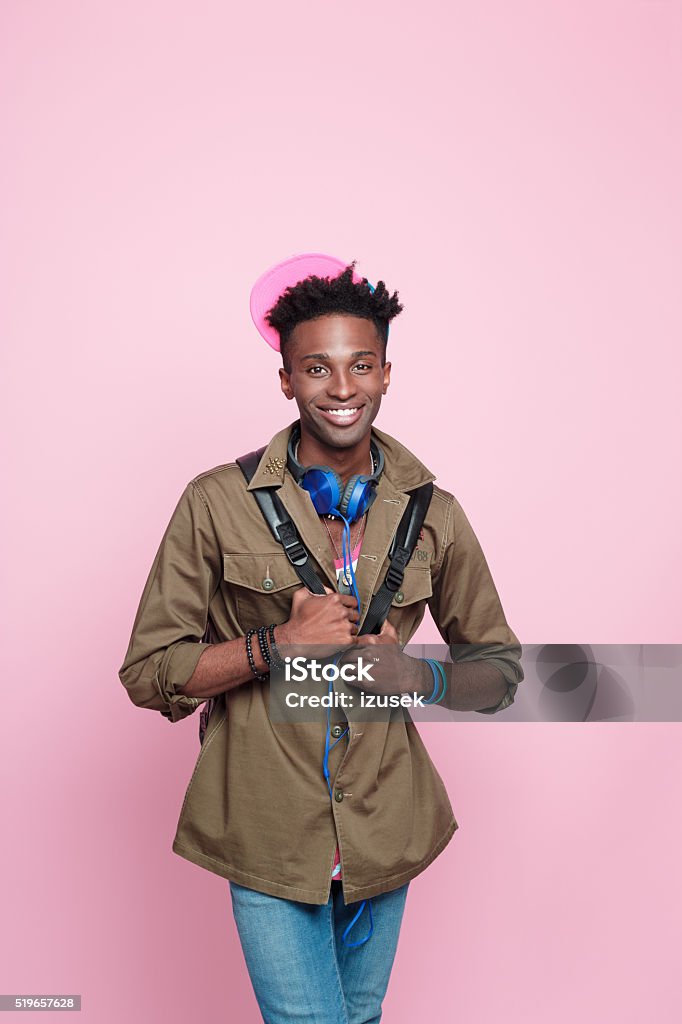 Smiling afro american guy, Studio portrait, pink background Studio portrait of cute afro american young man wearing headphone, standing against pink background and smiling at the camera. Adult Stock Photo