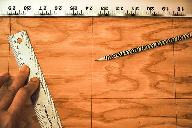 Two rulers and a pencil on top of a piece of plywood with measurement lines.