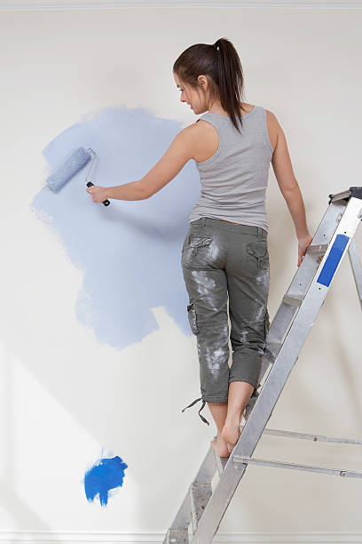 istock Woman Painting Wall With Paintroller While Standing On Stepladde 519661465