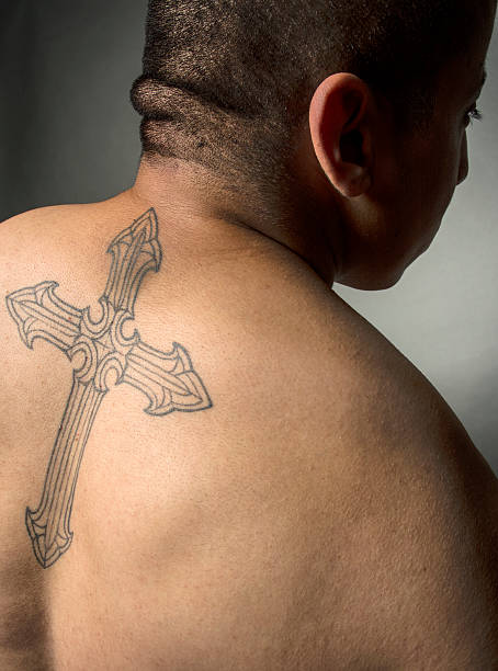 Hispanic Male With Religious Cross Tattoo On Back Hispanic Male With Religious Cross Tattoo On Back cross shoulder tattoos stock pictures, royalty-free photos & images