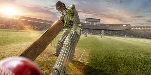Cricket Batsman Hitting Ball During Cricket Match In Stadium A close up image of a professional cricketer playing in batsman position wearing cricket whites and safety helmet, having just hit a ball during a cricket match in an outdoor stadium full of spectators. The action occurs under an evening sky at sunset. Stadium is fake, created from photographic and CG elements.  batsman photos stock pictures, royalty-free photos & images