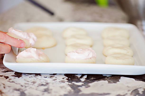 Frosting a sugar cookie Frosting sugar cookies with soft pink frosting for baby christening party. white sugar cookie stock pictures, royalty-free photos & images