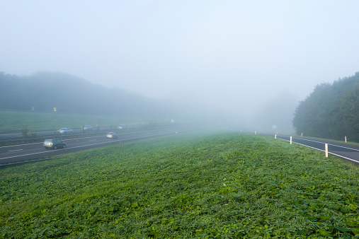 Passenger cars driving on a freeway in the Netherlands early on a foggy morning in the fall season.