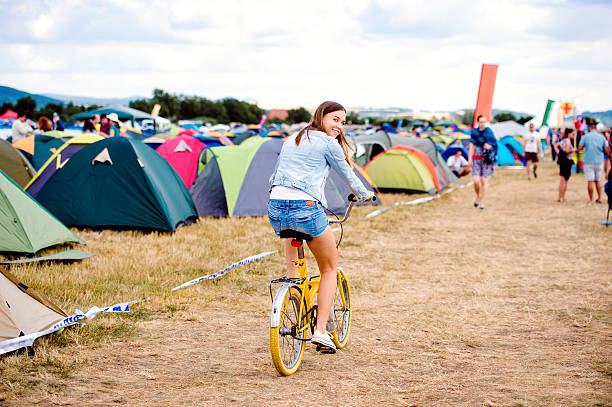 Teenage girl riding yellow bike at summer music festival Teenage girl having fun riding yellow bike at summer music festival in a tent sector, back view, rear viewpoint music festival camping summer vacations stock pictures, royalty-free photos & images