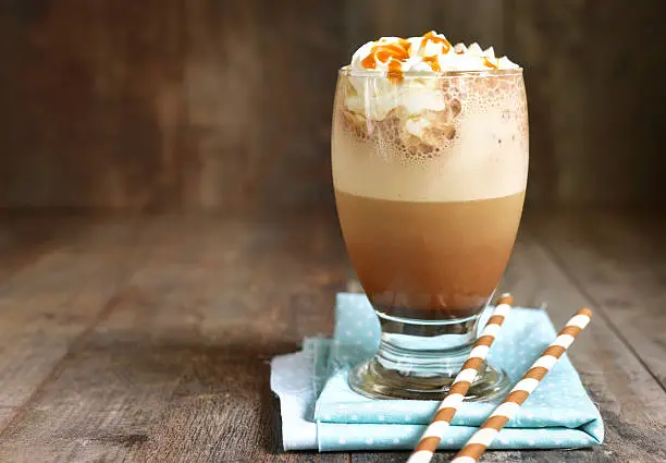 Frappuccino with caramel syrup and whipped cream in a glass on rustic background.