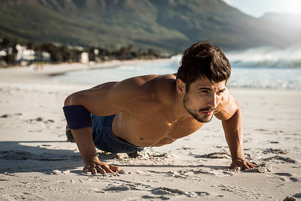 fit man doing push ups on the beach stock photo