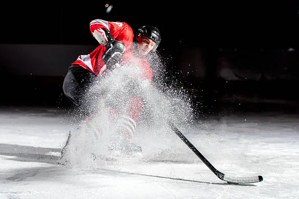 Ice hockey player shooting puck and ice powder spreading in ice hockey stadium.