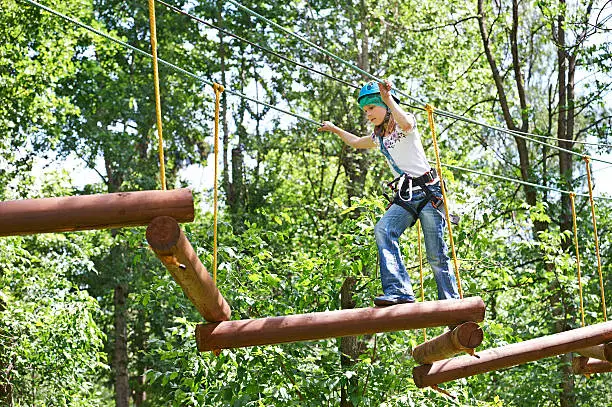 Girl is climbing to high rope structures in forest