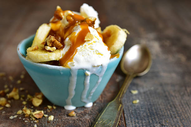 Vanilla ice cream with walnuts,banana and caramel in a blue bowl on a rustic wooden background.
