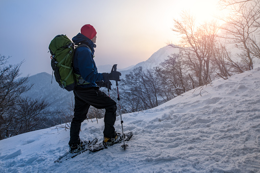 A man enjoys sunrise while snowshoeing through a forest in Japan