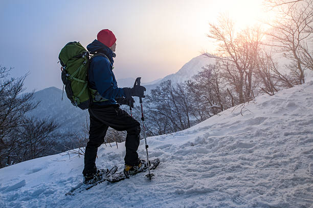 homem oferece nascer do sol, e caminhadas com raqueta de neve, através de uma floresta - snowshoeing winter sport snowshoe hiking - fotografias e filmes do acervo