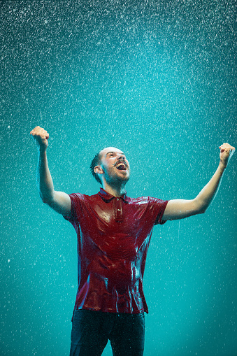 The portrait of young man in the rain. The man screaming on a turquoise background