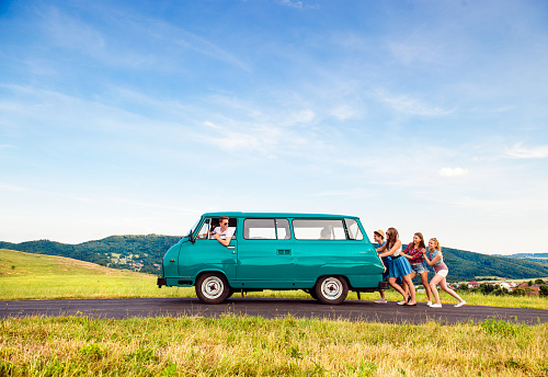 Young teenage hipster frieds with campervan against green nature and blue sky, jumping