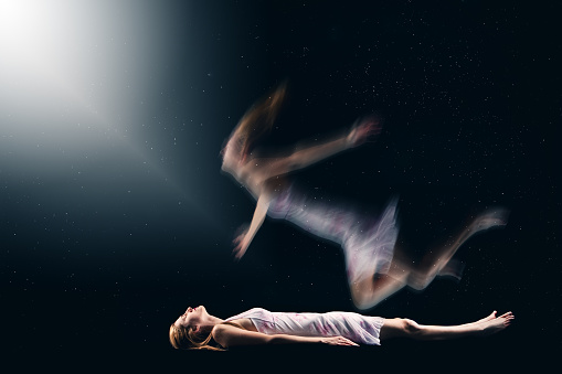 A concept image of a woman's spirit drifting from her body and floating towards a light.