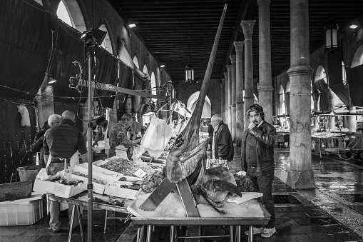 Venice, Italy - 5 April 2016:  Monochrome image of fishmongers setting up their stalls with a variety of fresh fish, including giant swordfish, at the Rialto fish market, Venice, Italy