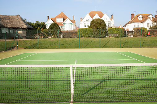 empty artificial grass tennis courts sunny day essex england, with thatched clubhouse - view from net 