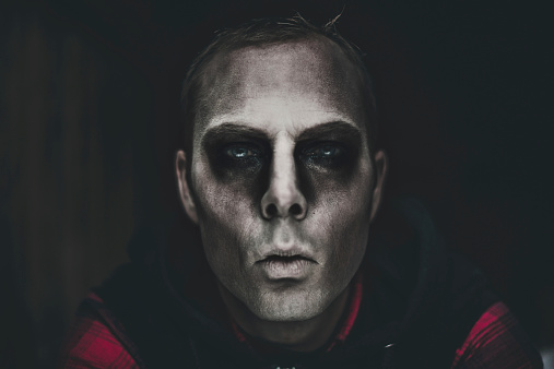 Picture of man with halloween make-up coming out of the dark. Dark and a bit scary.