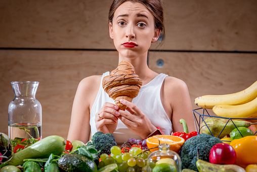 Young woman feeling sorry for eating sweet croissant instead of healthy fruits and vegetables. Worry about calories and weight