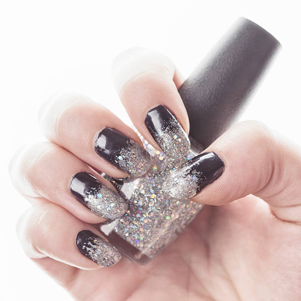 Manicured fingernails holding bottle of nail polish.