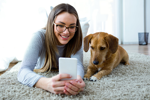 Portrait of beautiful young woman with her dog using mobile phone at home.