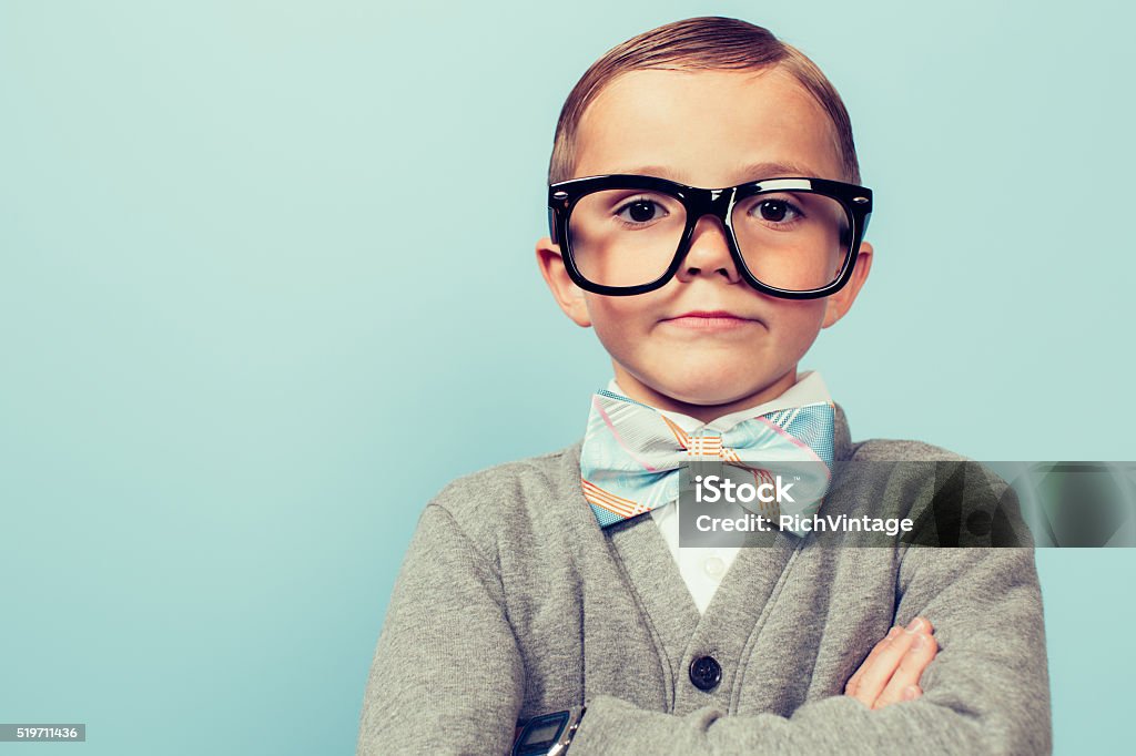 Young Nerd Boy Folding Arms and Blank Expression A young nerd boy with glasses sits with a blank expression on his face. He is wearing a bow tie and glasses and has an indifferent expression on his face. Retro styled   Nerd Stock Photo