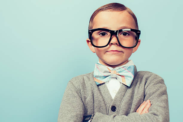 Young Nerd Boy Folding Arms and Blank Expression A young nerd boy with glasses sits with a blank expression on his face. He is wearing a bow tie and glasses and has an indifferent expression on his face. Retro styled   nerd sweater stock pictures, royalty-free photos & images
