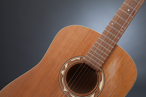 A detail shot of a neck of a western guitarin front of a grey background.