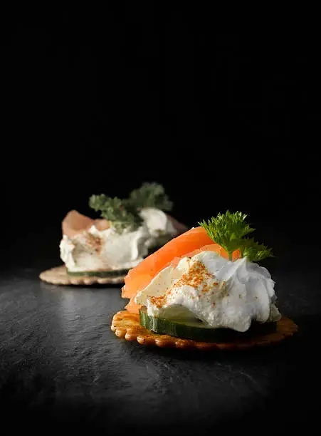 Creatively lit smoked salmon canapes against a black background. Copy space.
